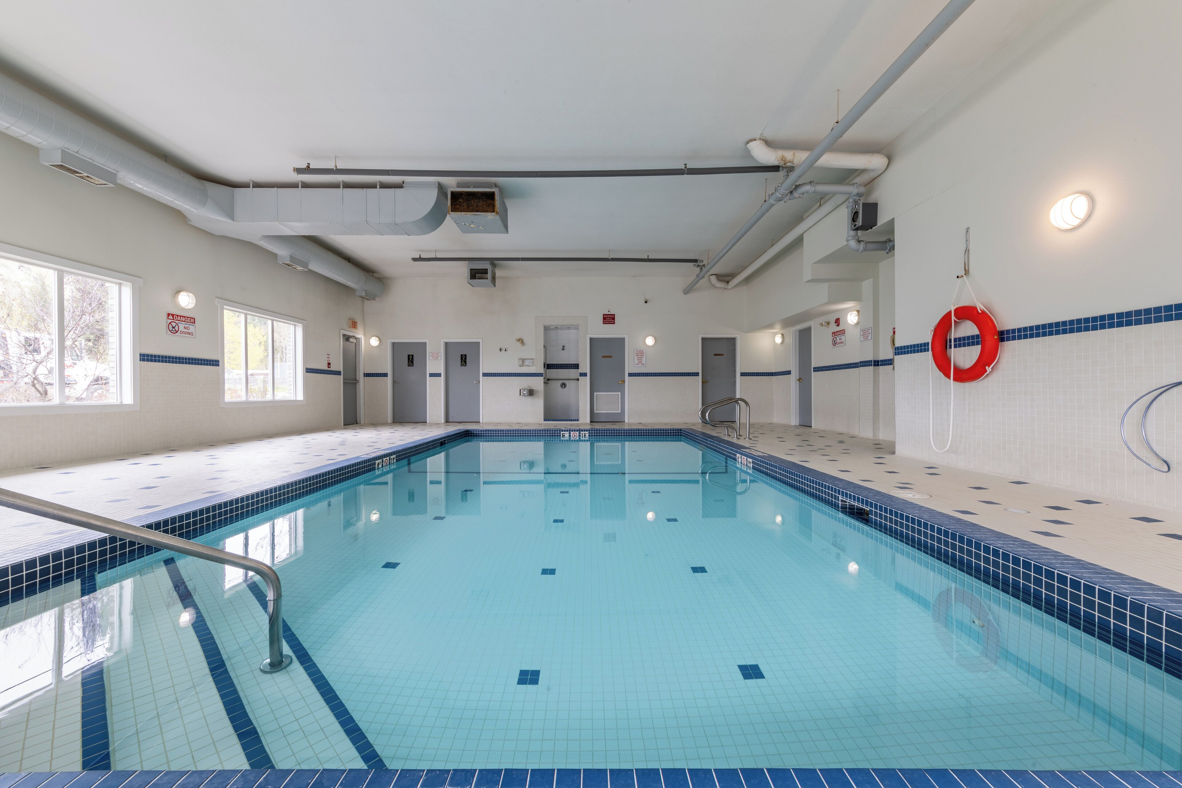 Une piscine avec un sol et des murs carrelés, une bouée de sauvetage accrochée au mur et une porte visible au fond.