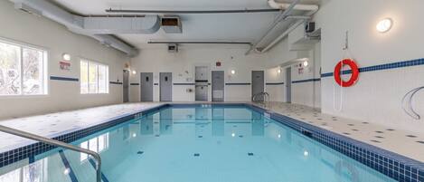 Une piscine avec un sol et des murs carrelés, une bouée de sauvetage accrochée au mur et une porte visible au fond.
