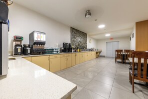 A modern kitchen with a coffee station, a large island, and a dining area with wooden chairs. - Ramada Limited Golden (Golden)