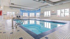 Una piscina interior con agua cristalina, suelo de baldosas y ventanas que dejan entrar luz natural.