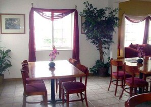 A dining area with a wooden table and chairs, a potted plant, and a sofa.