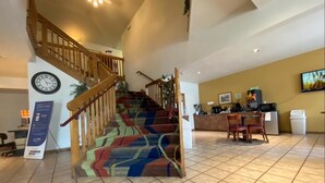 A hotel lobby with a staircase, a reception desk, and a kitchen area.