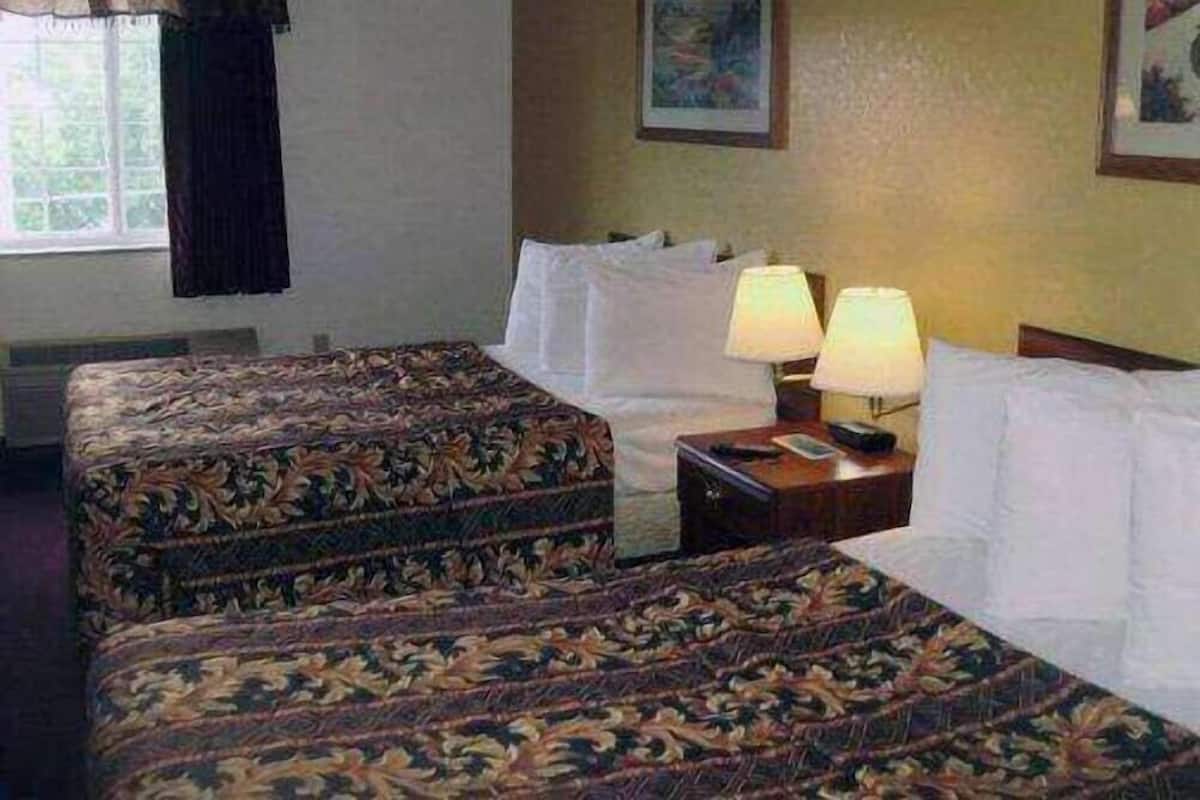 A hotel room with two beds, a nightstand with lamps, a window with curtains, and a painting on the wall.