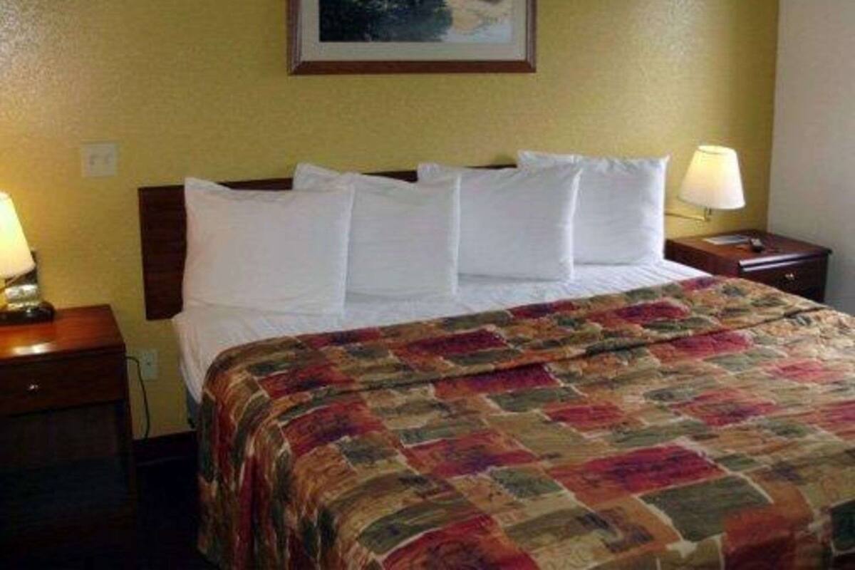 A hotel room with a bed, two bedside lamps, a nightstand, and a framed picture on the wall.
