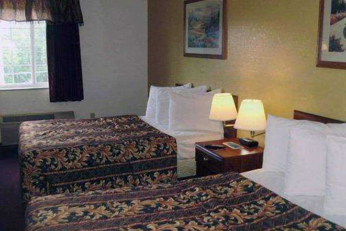 A hotel room with two beds, a nightstand with lamps, and a window with curtains.