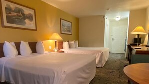 A hotel room with two beds, a desk, a chair, and a lamp.