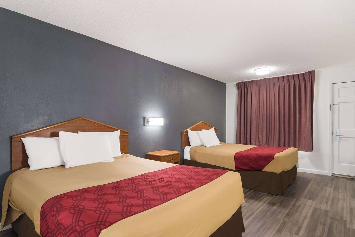 Habitación de hotel con dos camas, cabecero de madera, mesita de noche y ventana con cortinas.