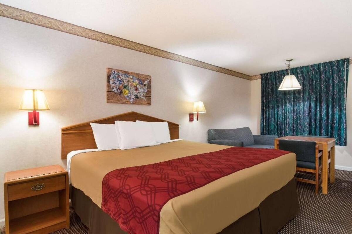 Habitación de hotel con cama, dos lámparas de noche, escritorio, una silla y un adorno en la pared.