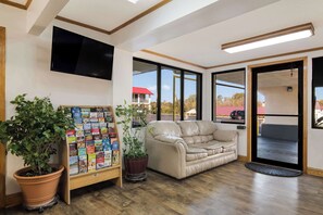 A lobby with a beige sofa, a bookshelf, and a large window offering a view of the outside. - Econo Lodge Calhoun North Damascus (Calhoun)