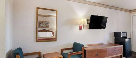 A hotel room with a bed, two chairs, a small table, a dresser, a television, a lamp, and a microwave.
