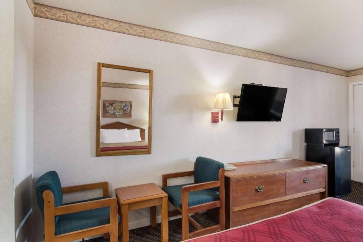 Habitación de hotel con cama, dos sillas, una mesita, televisión, lámpara y microondas.