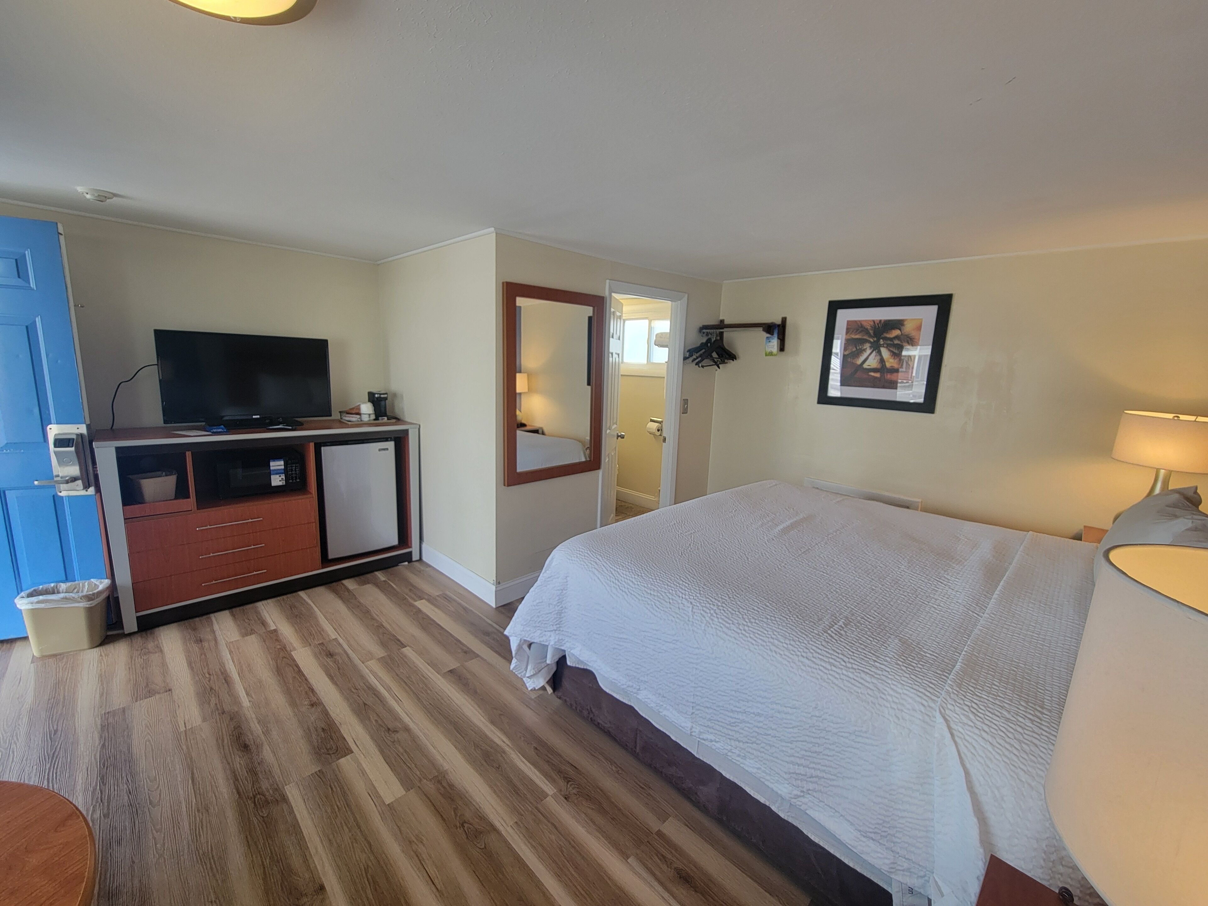 A hotel room with a bed, a desk with a television, a small refrigerator, and a mirror.