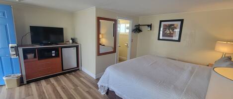 A hotel room with a bed, a desk with a television, a small refrigerator, and a mirror.