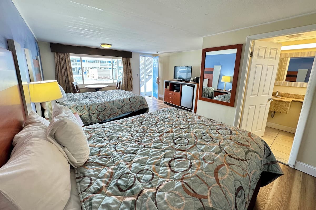 A hotel room with two beds, a desk with a television, a mirror, and a bathroom visible through an open door.