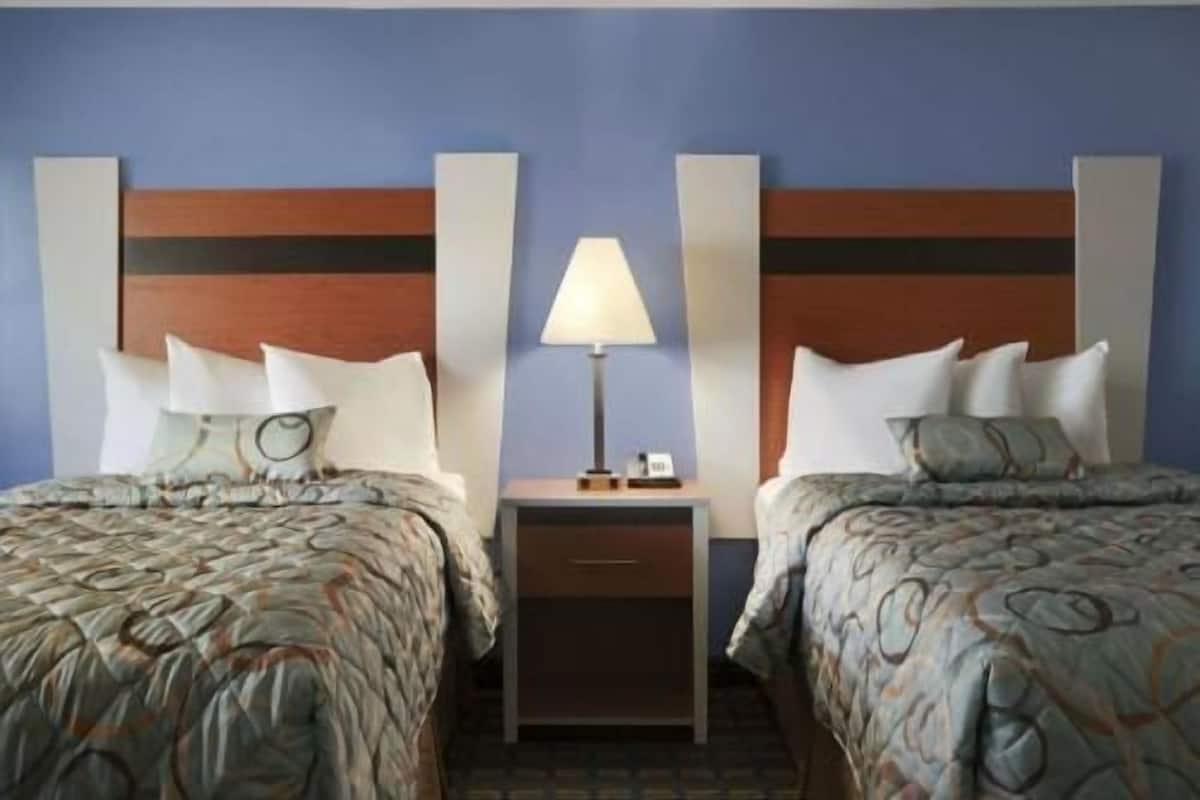 A hotel room with two beds, a nightstand with a lamp, and a wall-mounted telephone.