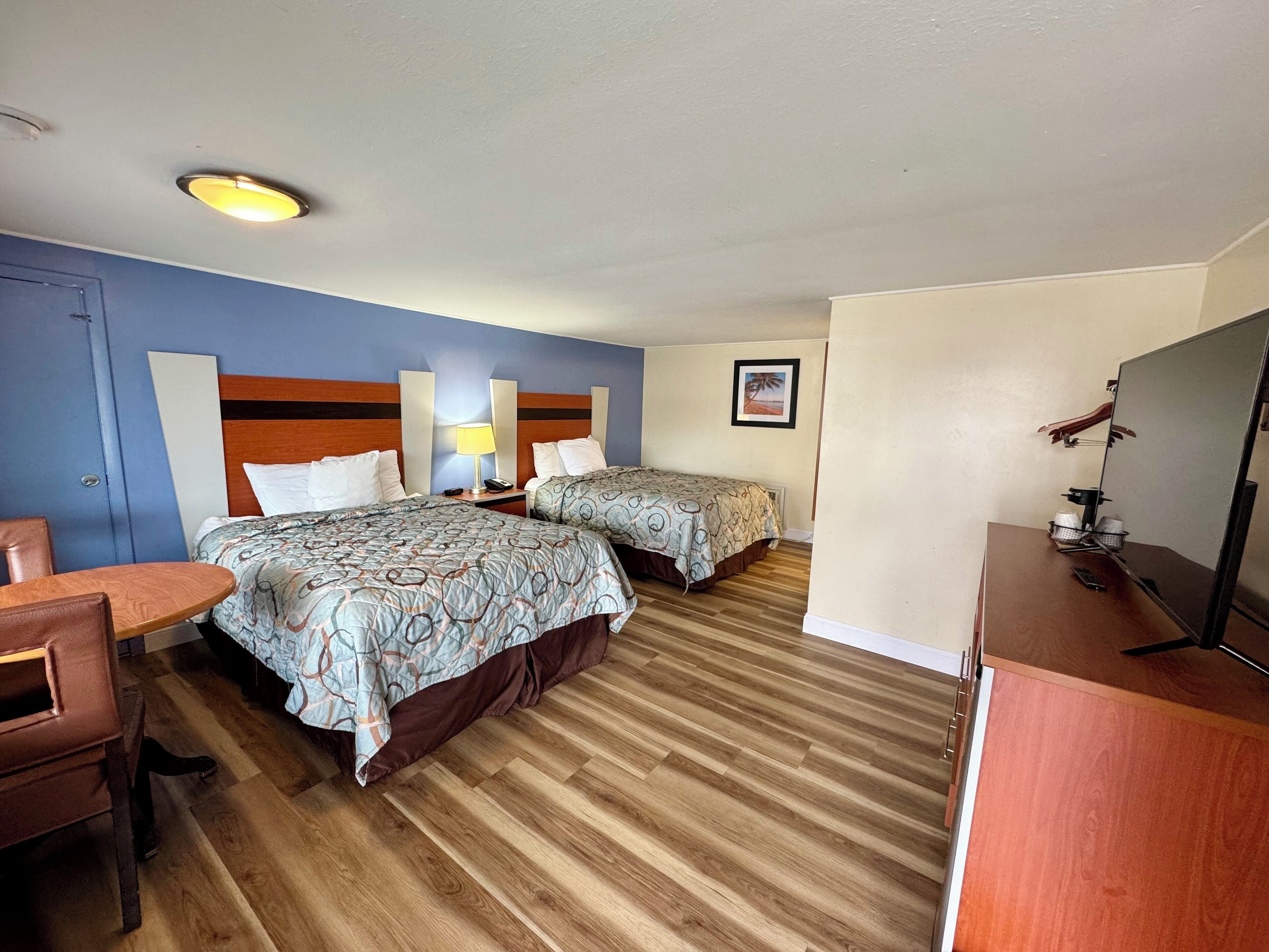 A hotel room with two beds, a desk, a chair, a TV, and a framed picture on the wall.
