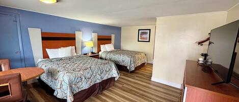 A hotel room with two beds, a desk, a chair, a TV, and a framed picture on the wall.