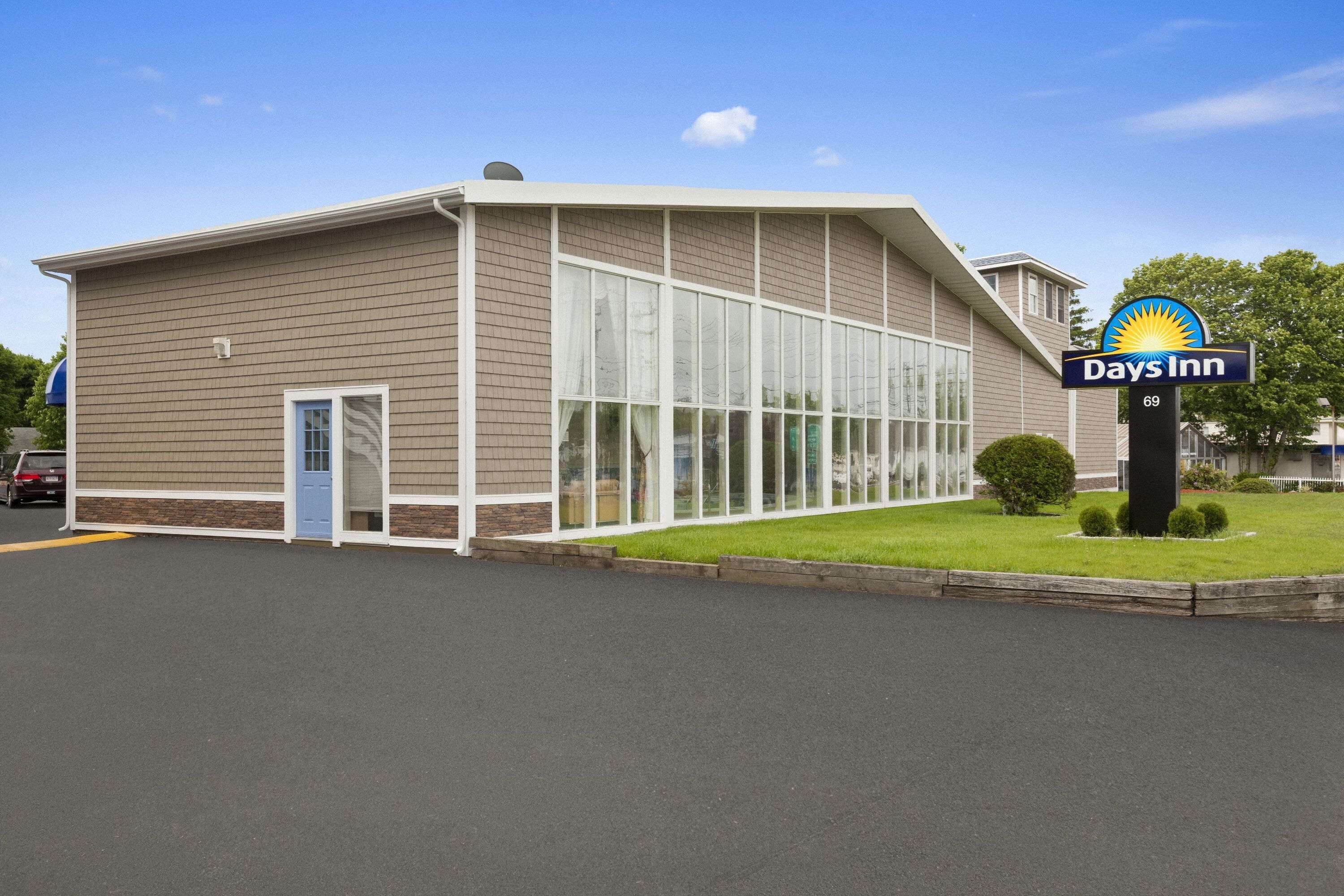 A Days Inn building with a large glass window section, a blue door, and a parking lot in front.