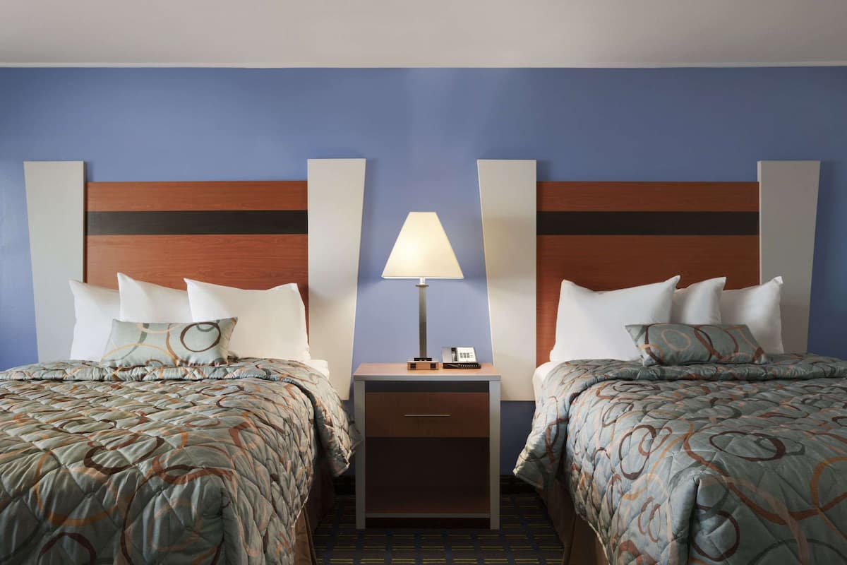 A hotel room with two beds, a nightstand with a lamp, and a wooden headboard.
