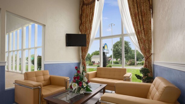 A hotel room with two beige sofas, a glass coffee table, and a flat-screen TV mounted on the wall. - Days Inn by Wyndham West Yarmouth/Hyannis Cape Cod Area (West Yarmouth)