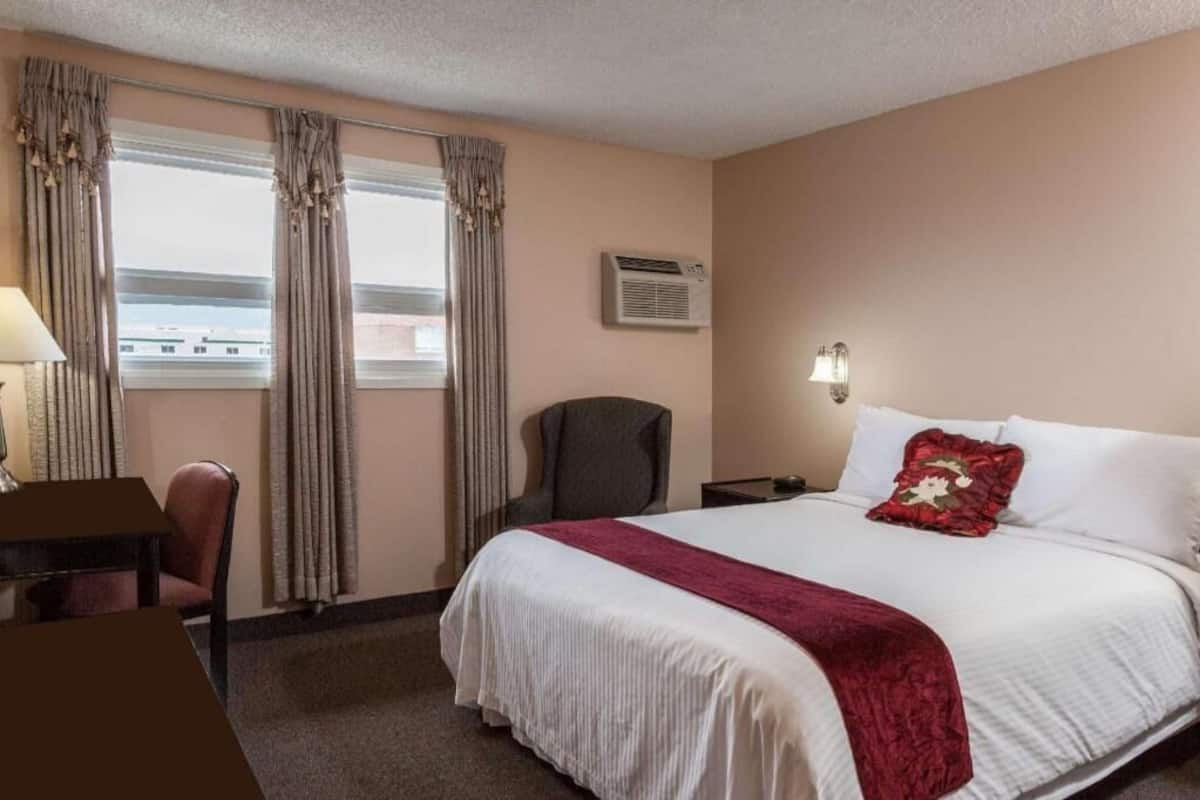 Une chambre d’hôtel équipée d’un lit, d’un bureau, d’une chaise, d’un climatiseur et de rideaux.