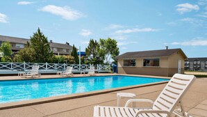 A swimming pool with lounge chairs and a small building, surrounded by trees and residential buildings. - Days Inn by Wyndham Fredericton (Fredericton)