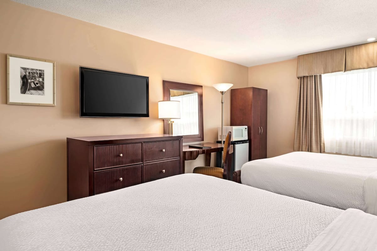 Une chambre d’hôtel avec deux lits, un bureau, une télévision, un miroir et une armoire.