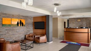 A lobby with leather chairs, a reception desk, a flat-screen TV, and a wall with a sunset painting. - Days Inn by Wyndham Fredericton (Fredericton)
