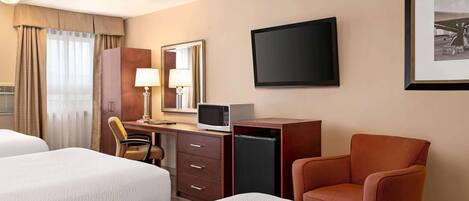 A hotel room with two beds, a desk with a computer, a television, and a framed picture on the wall.