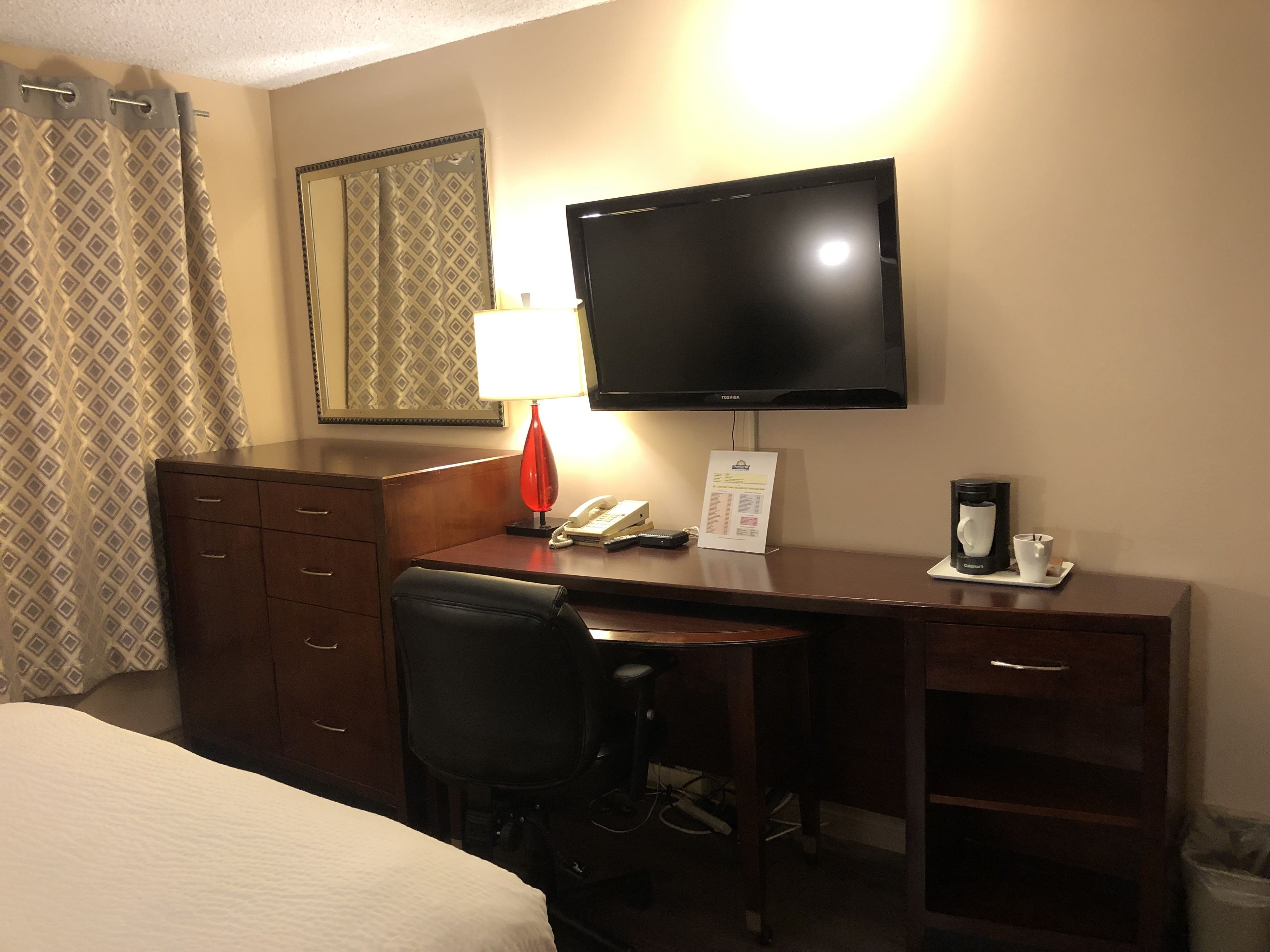 A hotel room with a bed, a desk, a chair, a TV, a lamp, a telephone, a coffee maker, and a trash bin.