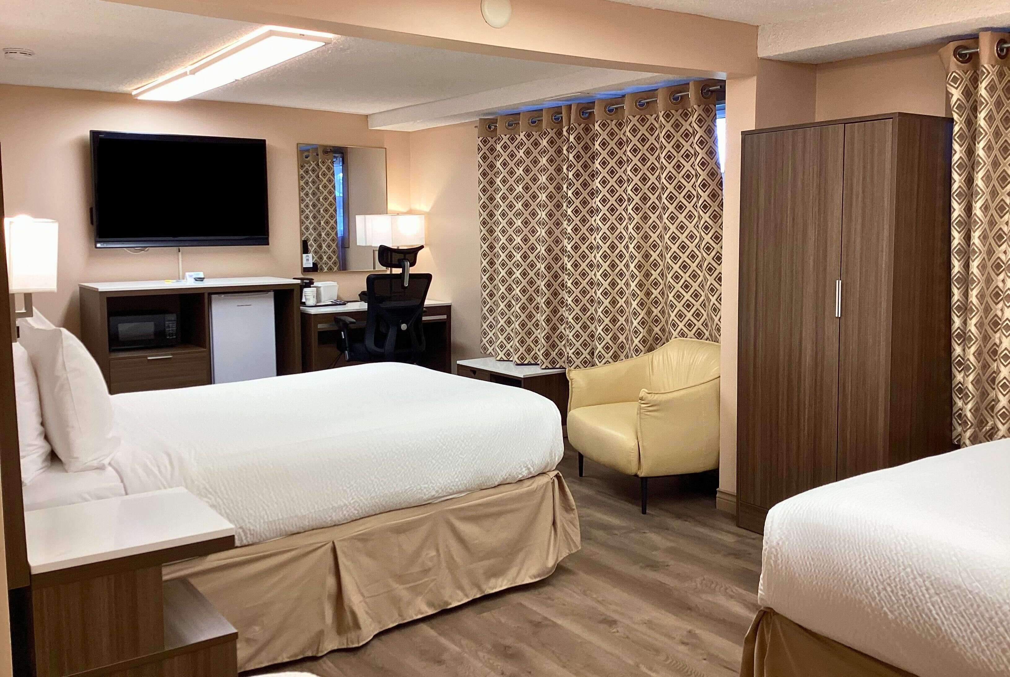 A hotel room with a bed, desk, chair, TV, wardrobe, and patterned curtains.