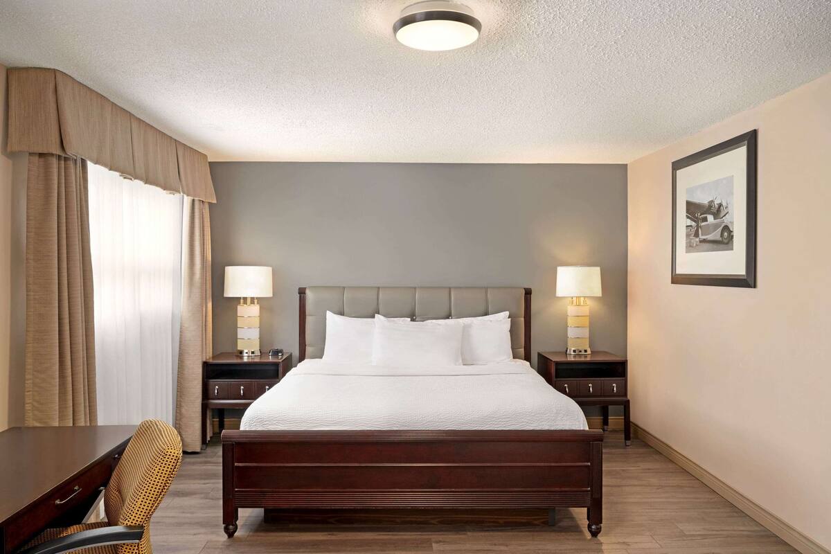 Une chambre d’hôtel avec un grand lit, deux tables de chevet avec des lampes, un bureau, une chaise et un tableau encadré au mur.