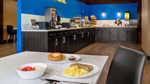 A breakfast area with a counter, a bowl of fruit, a plate with scrambled eggs and sausage, and a sign that reads "Breakfast is on us." - Days Inn by Wyndham Fredericton (Fredericton)