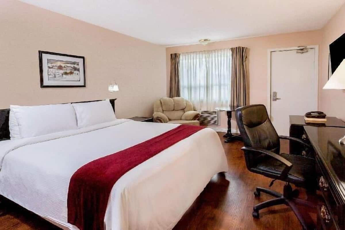 Una habitación de hotel con una cama, un escritorio, una silla, un ventanal con cortinas, una puerta y un cuadro en la pared.