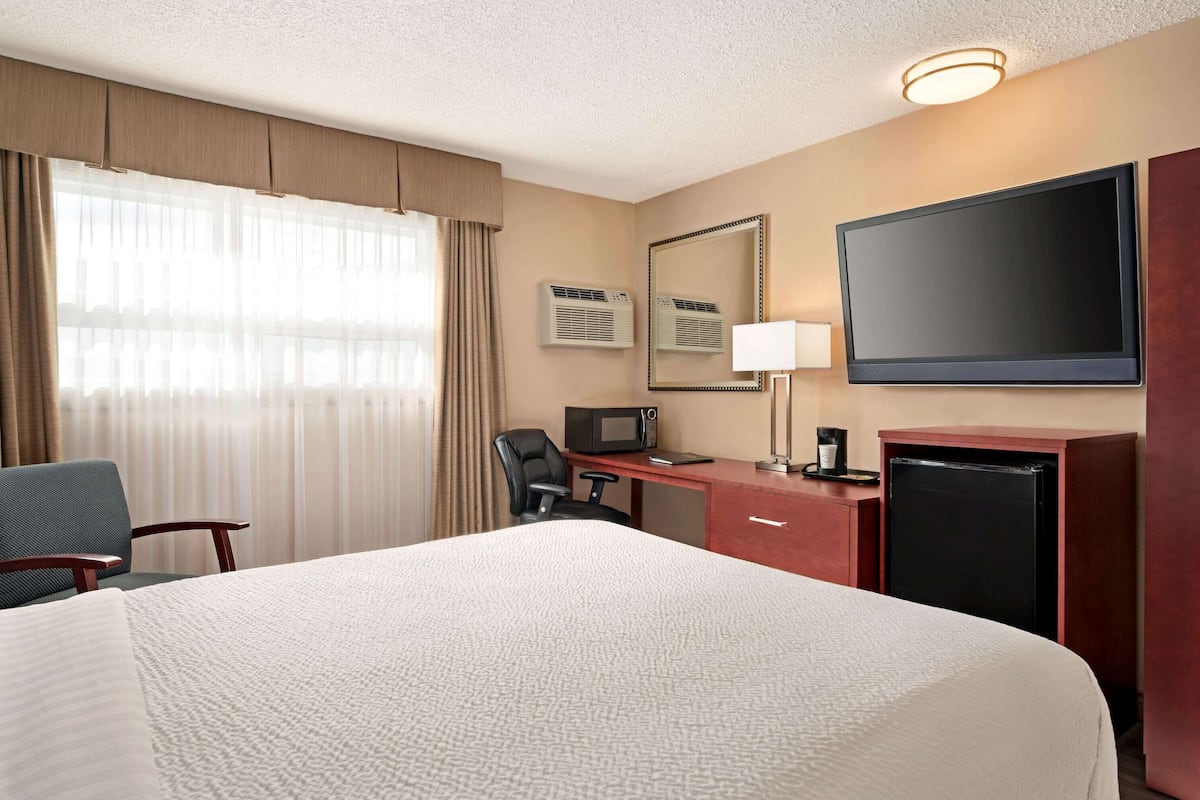 Une chambre d’hôtel avec un grand lit, un bureau avec un ordinateur, une télévision, un four à micro-ondes et un réfrigérateur.
