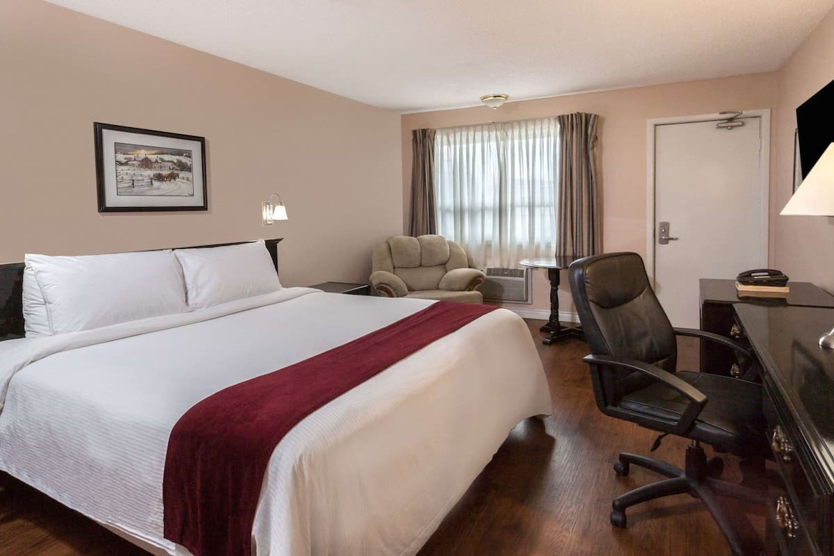 Une chambre d’hôtel avec un grand lit, un bureau, une chaise, une lampe et une fenêtre avec des rideaux.
