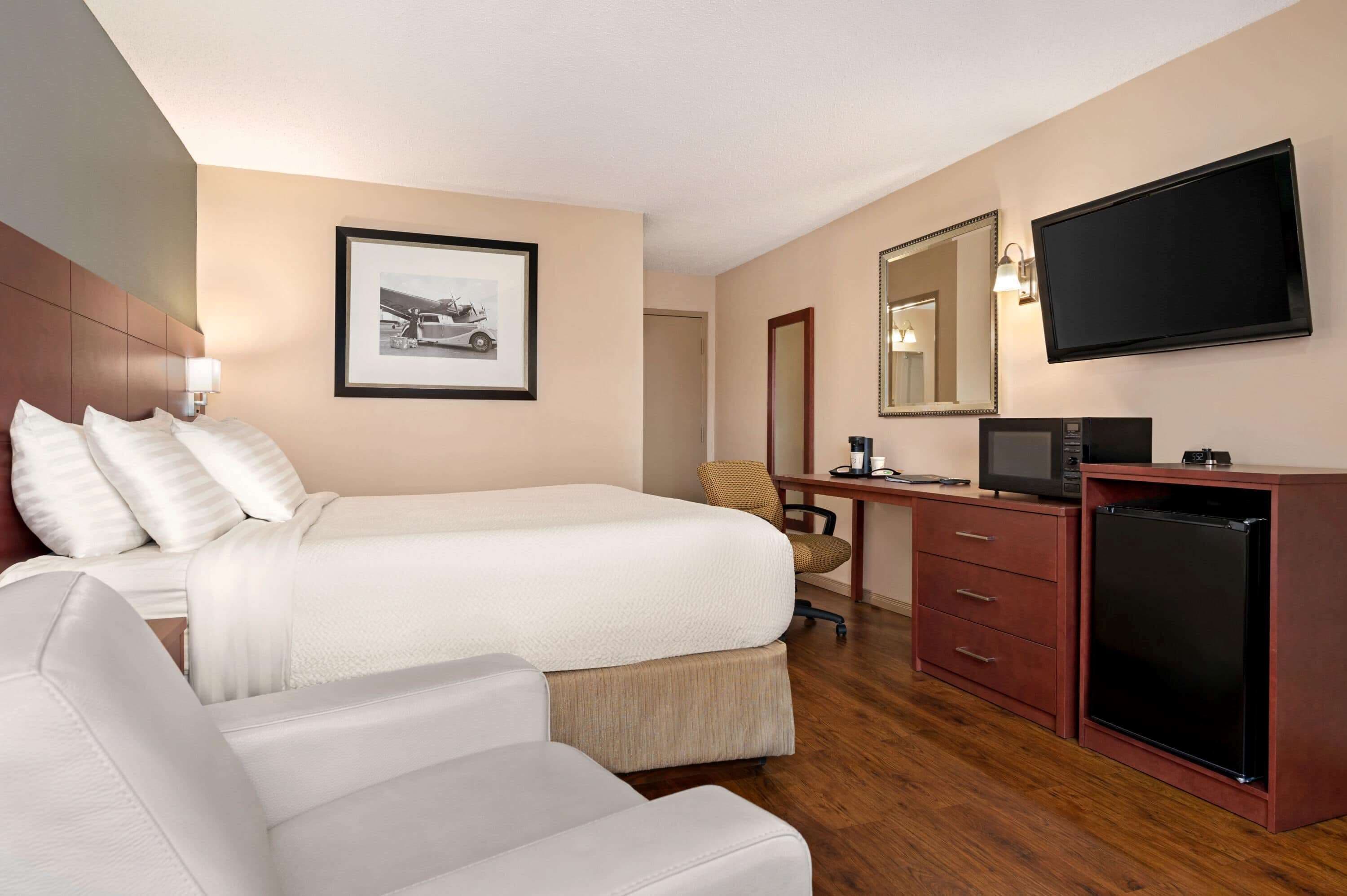 A hotel room with a bed, a desk with a computer, a TV, a refrigerator, and a chair.
