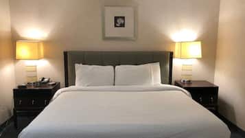 Habitación de hotel con una cama grande, dos mesitas de noche con lámparas, un cuadro en la pared y piso alfombrado.