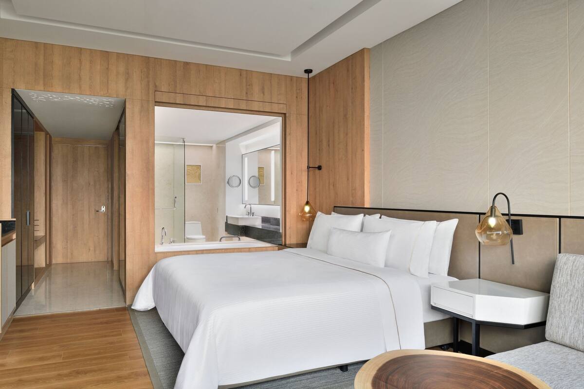 A modern hotel room with a large bed, a bedside table, a desk, and a mirror.