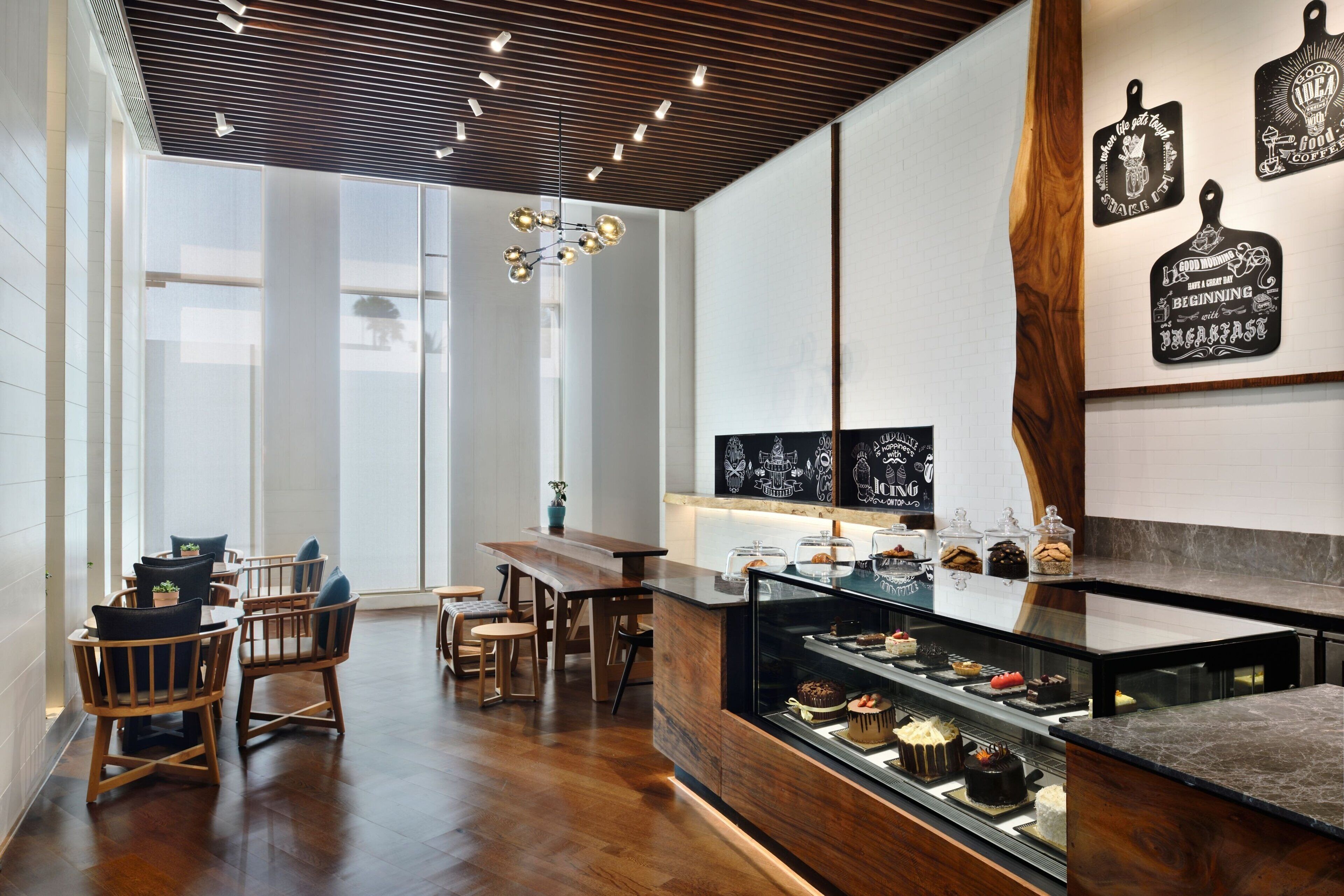 A modern cafe interior with wooden furniture, a central dining table, and a display case with desserts.