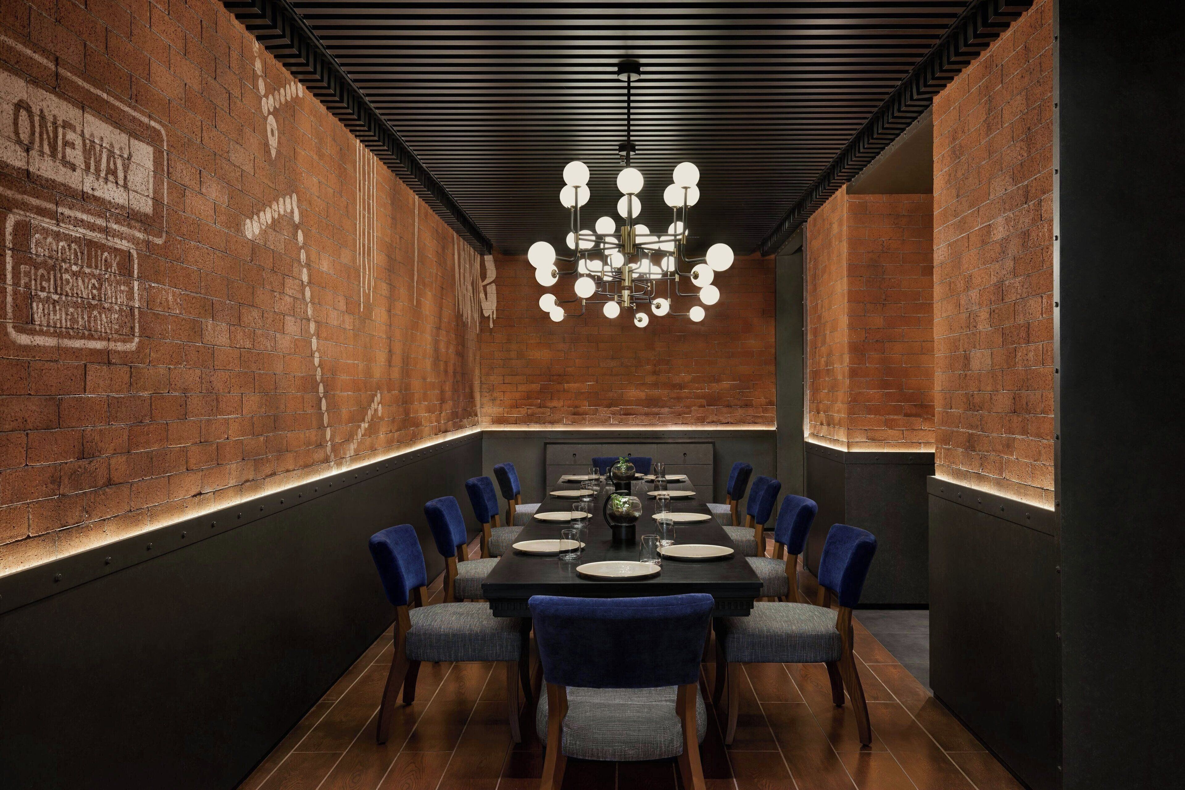A conference room with a brick wall, a chandelier, and a long table with chairs.