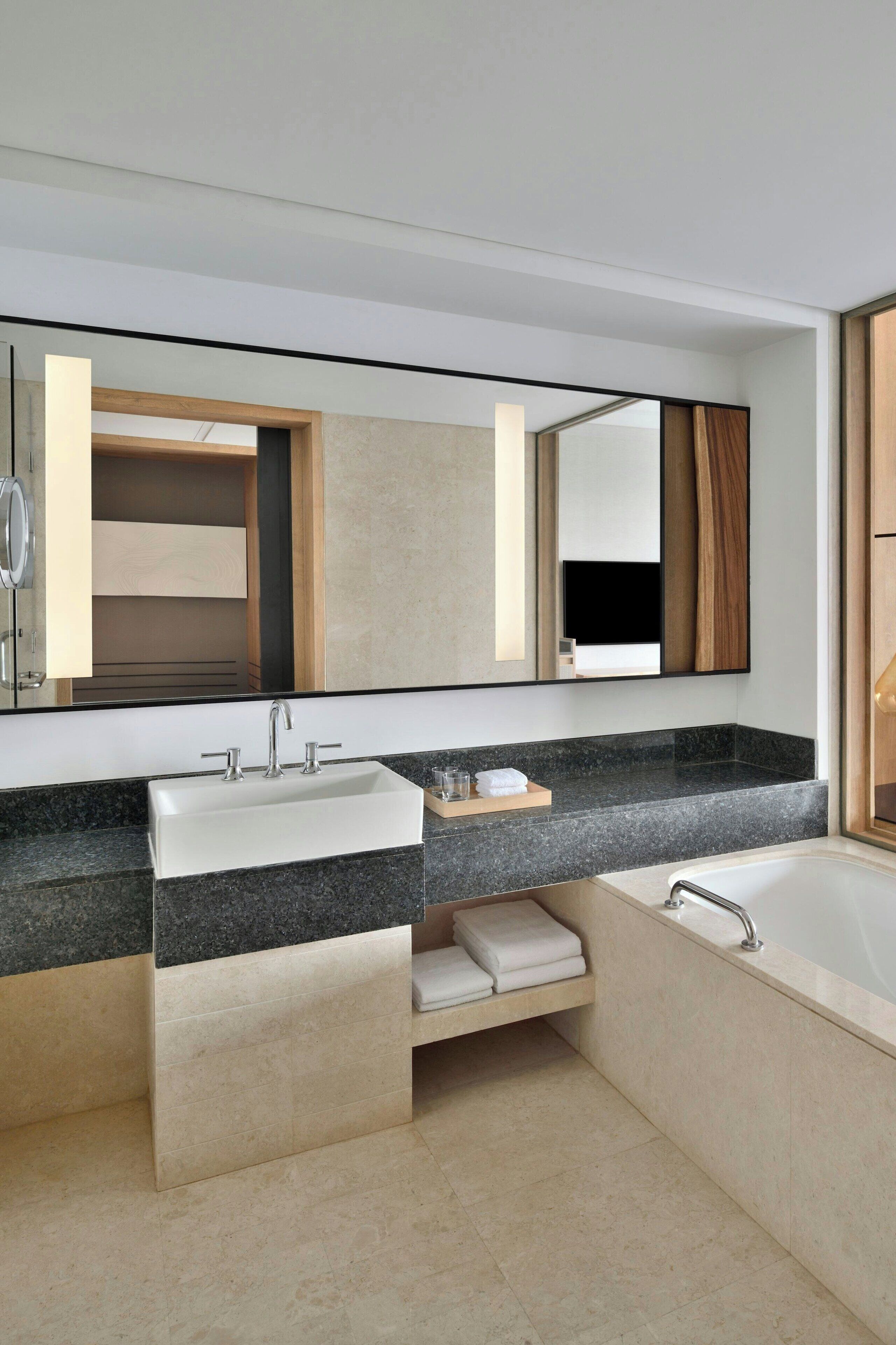 Un baño moderno con un espejo grande, dos lavamanos, una bañera y un perchero para toallas.