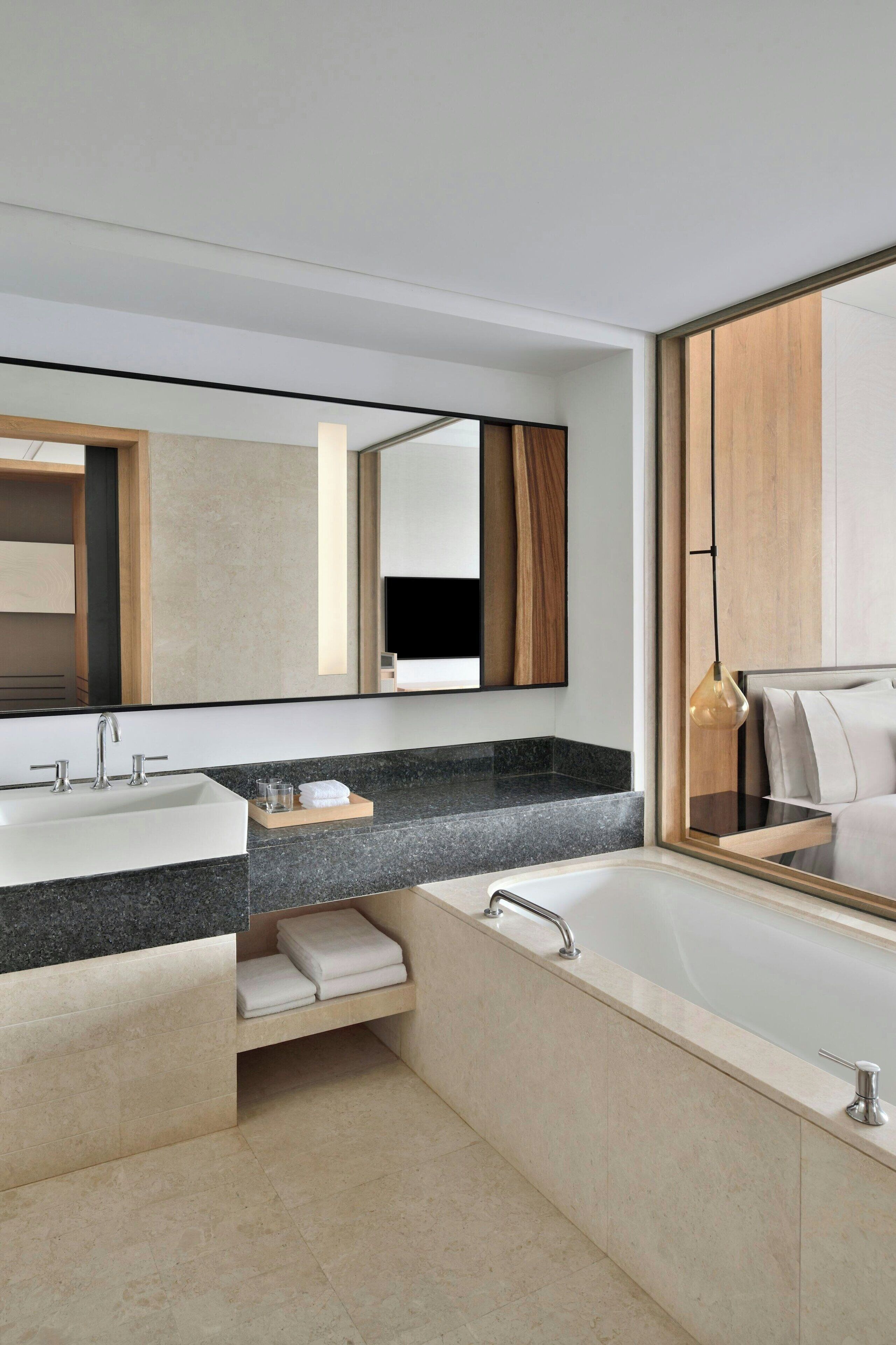 A modern bathroom with a double sink, a large mirror, and a bathtub.