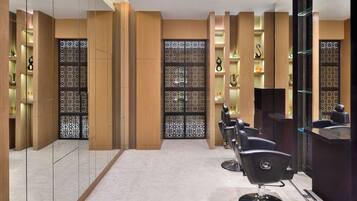 Un moderno salón de belleza con un diseño limpio y minimalista, que cuenta con una fila de sillones de peluquería, una zona de recepción y estanterías decorativas con diversos objetos.
