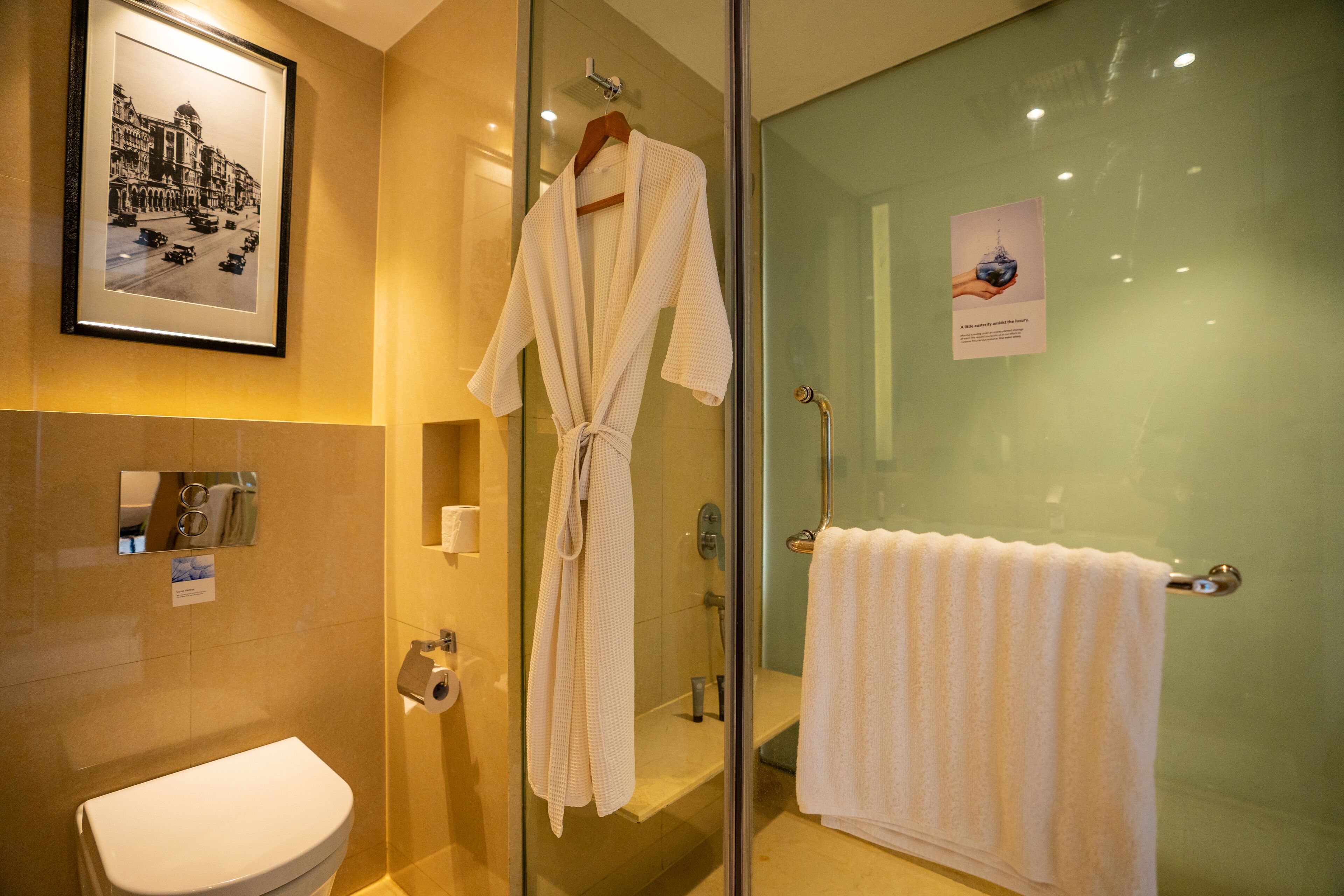 Une salle de bain comprenant des toilettes, une douche en verre, une robe suspendue à un porte-manteau et une serviette sur un porte-serviettes.