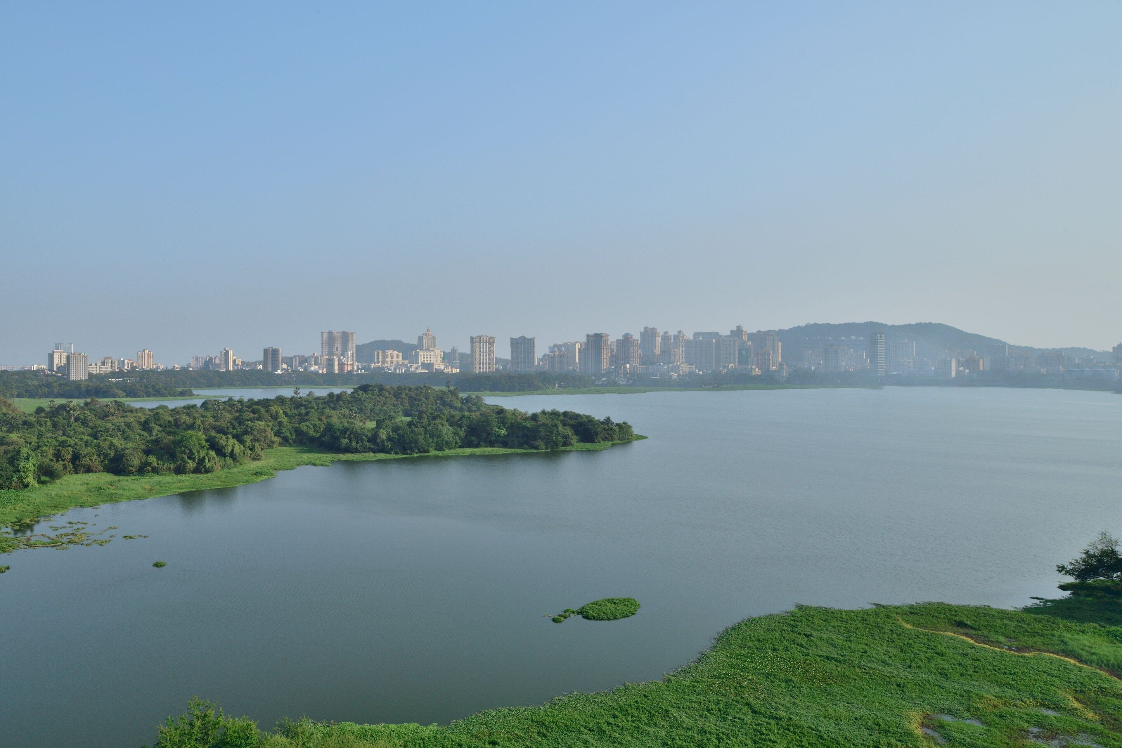 A panoramic view of a city skyline across a calm lake with a small island in the foreground.