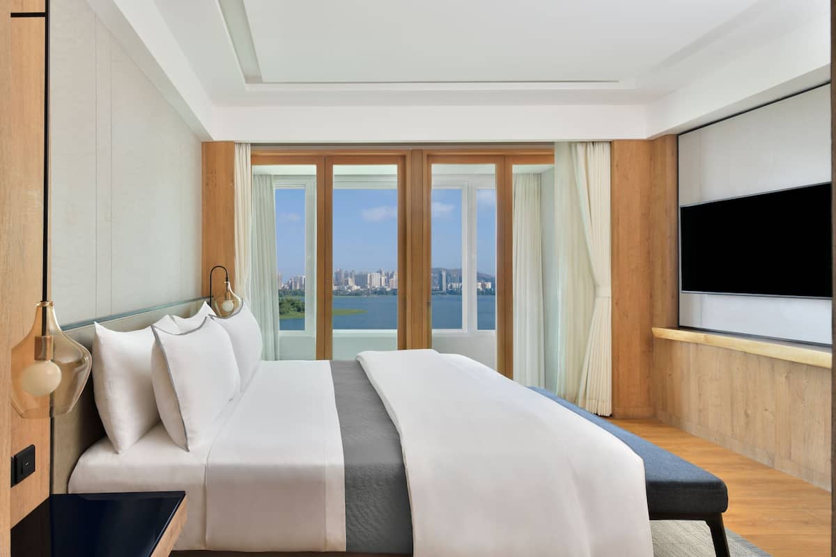 A modern hotel room with a large bed, a TV, and a city view.