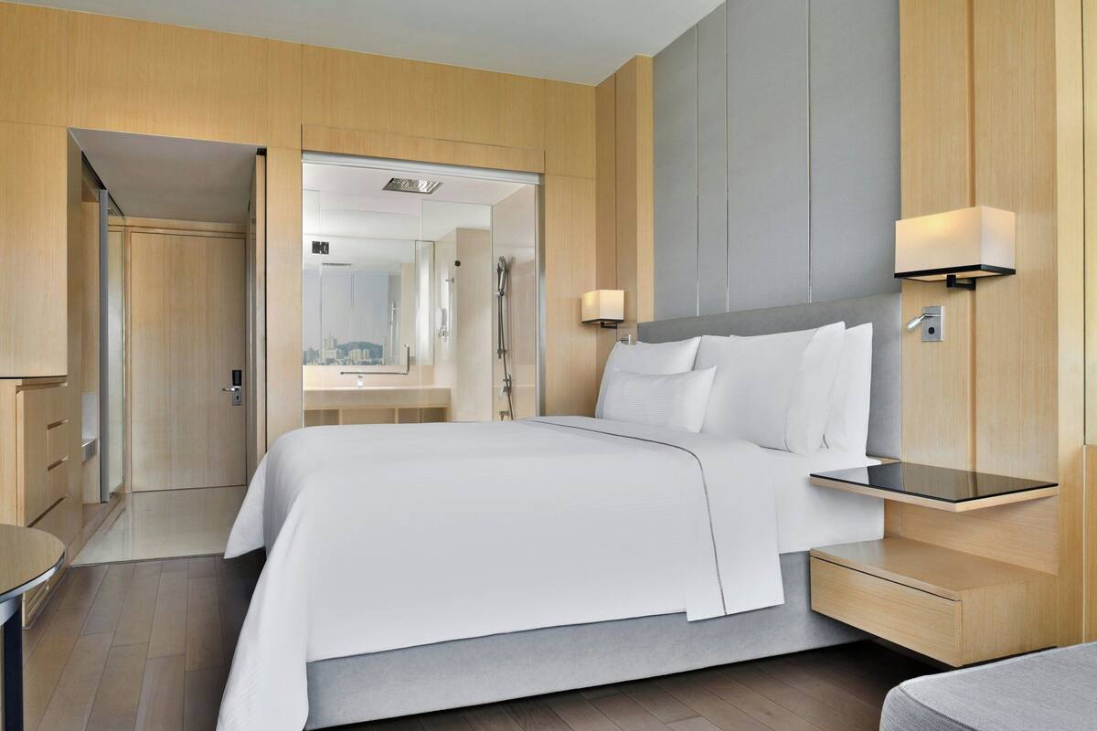 A modern hotel room with a large bed, a bedside table, a nightstand, a mirror, and a view of the bathroom.