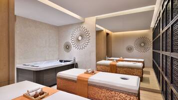 A spa room with two massage beds, a large bathtub, and decorative wall art.