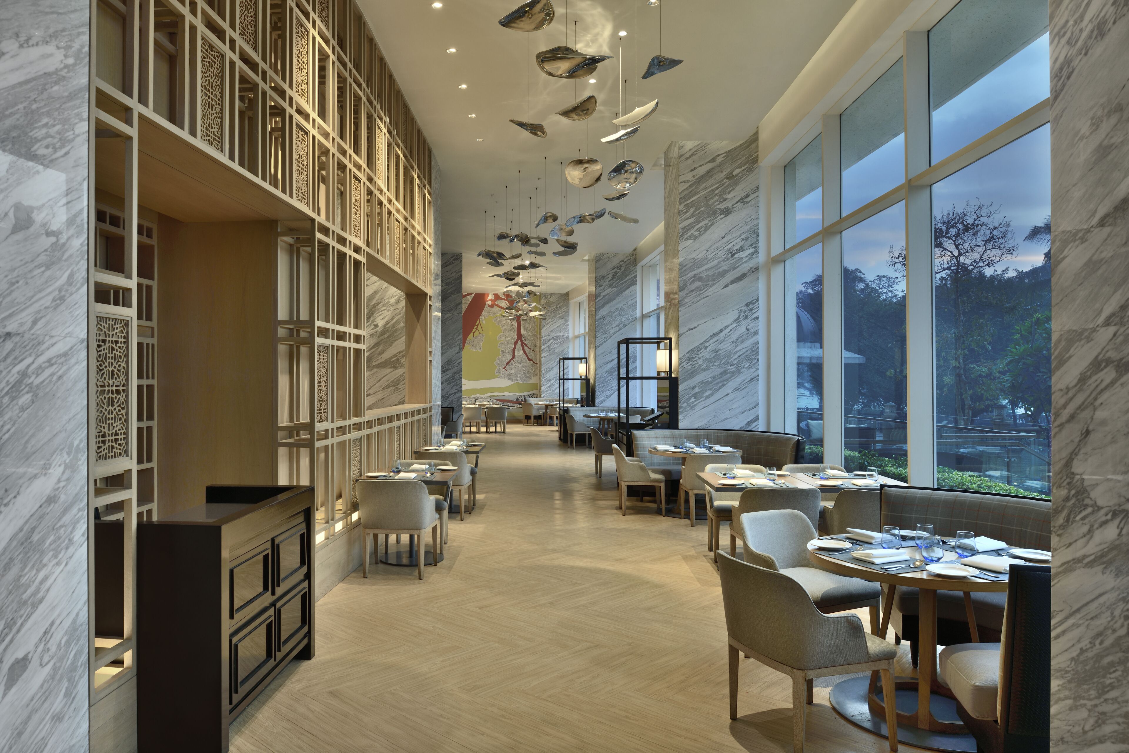 A spacious restaurant with high ceilings, marble walls, and large windows offering a view of the outdoors.